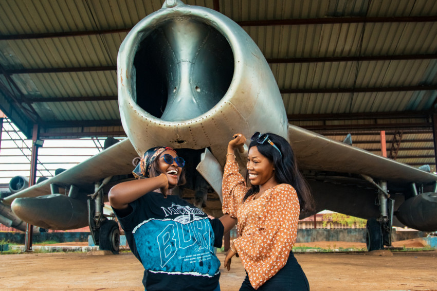 Two happy friends beneath a war plane