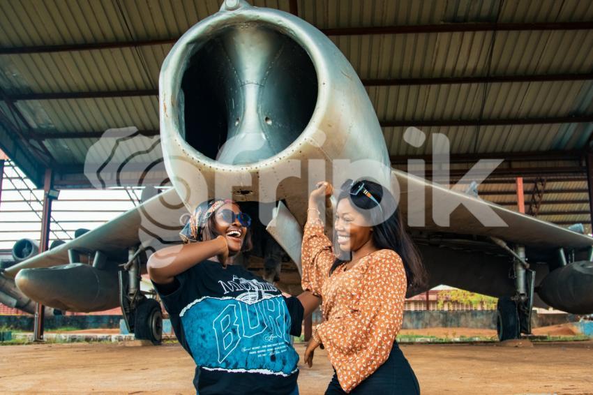 Two happy friends beneath a war plane