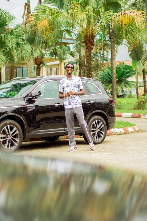 A happy boy standing in front of car